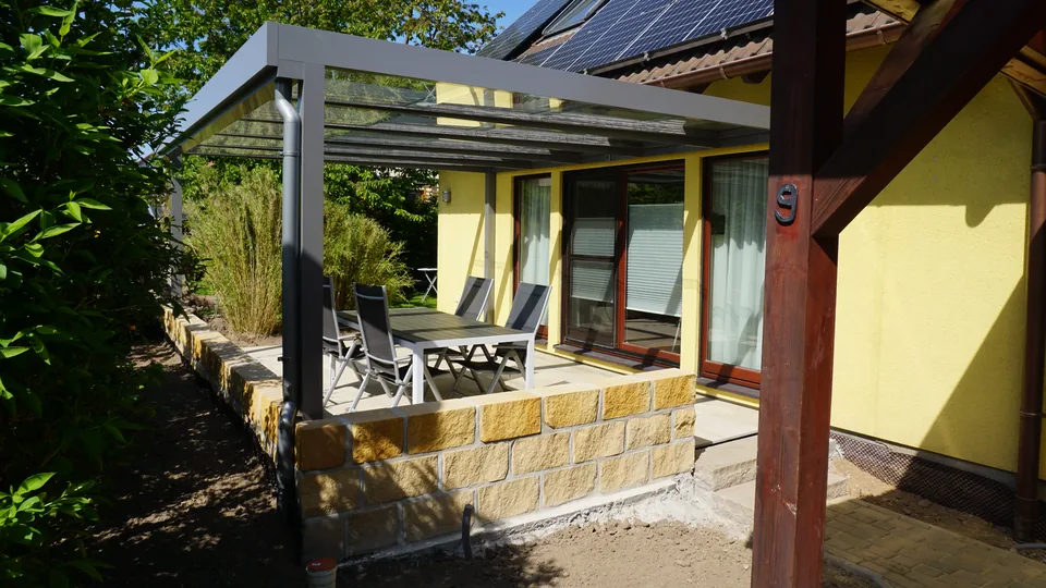 Terrasse mit Sandsteinmauer und Glasüberdachung an einem Wohnhaus