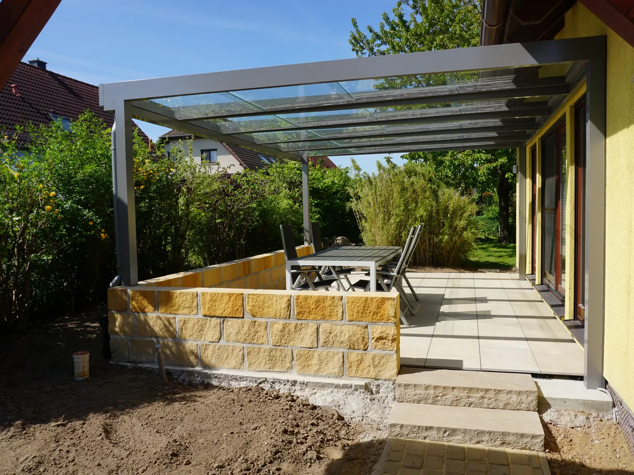 Fertige Terrasse mit Sandsteinmauer, Feinsteinplatten und Glasüberdachung in Moritzburg